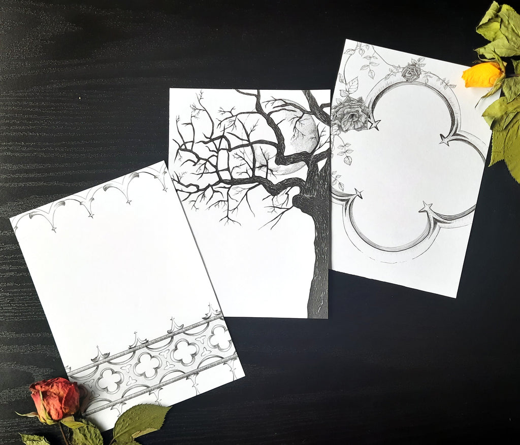 Three gothic themed black ink illustrations printed on white pages, laying on a dark background with two dried roses in the corners.