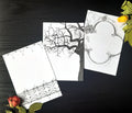 Three gothic themed black ink illustrations printed on white pages, laying on a dark background with two dried roses in the corners.