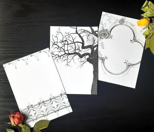 Three gothic themed black ink illustrations printed on white pages, laying on a dark background with two dried roses in the corners.